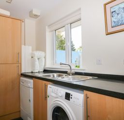A utility room with a washing machine dishwasher sink and cupboards under a window at Trevose House Crantock