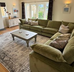 A living room with a green sofa and coffee table at Trevose House in Crantock