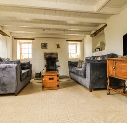 A living room with two gray sofas a wooden chest as a coffee table a stone fireplace and a wooden TV stand at Higher Roskorwell Cottage in St Keverne