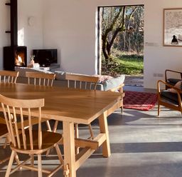 A dining area with wooden table and chairs next to a living space with sofa fireplace and armchairs at High Cogges Farm Holiday Cottages - The Cart Shed High Cogges near Witney