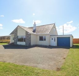A detached house with a stone and cream exterior a driveway and a blue garage door at Glanffraw in Aberffraw Ty Croes