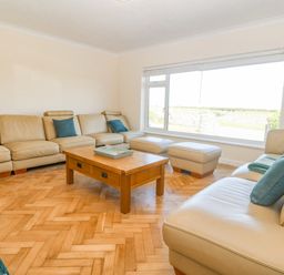 A living room with leather sofas and blue cushions around a wooden coffee table at Glanffraw in Aberffraw Ty Croes