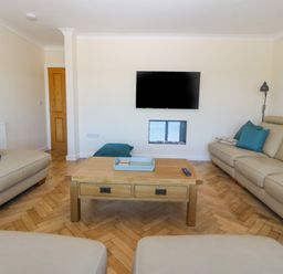 A living room with beige sofas blue cushions a wooden coffee table and a wall mounted TV at Glanffraw in Aberffraw Ty Croes