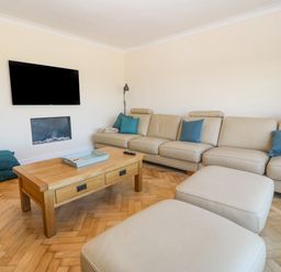 A living room with a beige sectional sofa and blue pillows a wooden coffee table a wall-mounted television and a fireplace at Glanffraw in Aberffraw Ty Croes