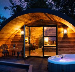 An arched wooden pod with a hot tub outside and a table with two chairs at The Piglet Pod in Llanarth