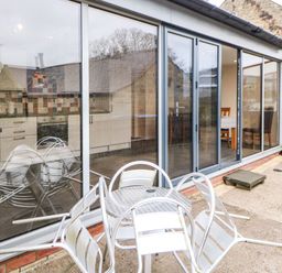 A patio with metal table and chairs outside a room with large glass sliding doors at Houghton North Farm Cottage in Heddon-on-the-Wall near Hexham