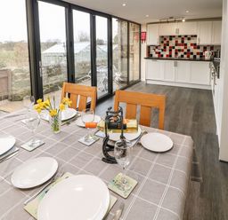 A dining table set with plates glasses and wine bottle next to a kitchen with white cabinets and black red white tiled backsplash at Houghton North Farm Cottage Heddon-on-the-Wall near Hexham