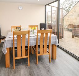 A dining room with a wooden table and chairs next to large glass sliding doors at Houghton North Farm Cottage in Heddon-on-the-Wall near Hexham