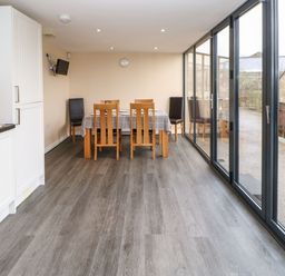 A dining area with a table covered by a checkered tablecloth and wooden and black chairs next to large glass sliding doors at Houghton North Farm Cottage in Heddon-on-the-Wall near Hexham