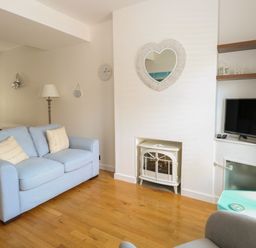 A living room with a blue sofa white fireplace and a wall-mounted television at Gulls Nest in Pakefield