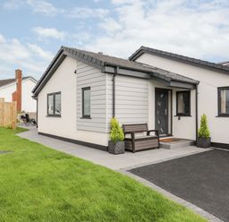The exterior of a single story house with grass lawn a bench near the front door and two potted plants at The Herun in Rhosneigr