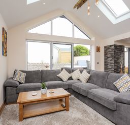 A living room with a grey L-shaped sofa a wooden coffee table and large windows at The Herun in Rhosneigr
