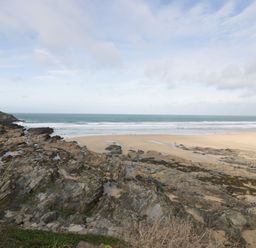 A rocky coastline with a sandy beach and ocean waves under a cloudy sky at Newquay Fistral Beach View in Newquay