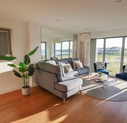 A living room with a gray sofa, two blue chairs, a coffee table, a floor lamp, a large mirror, and a plant at Newquay Fistral Beach View in Newquay