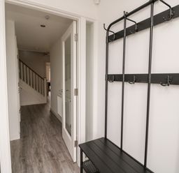 An entryway with a black coat rack and bench a hallway with a staircase at Amble Views in Amble