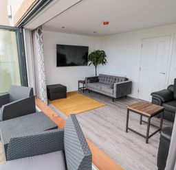 A living room with a gray sofa black armchairs yellow rug and outdoor seating area at Amble Views in Amble
