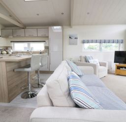 A combined kitchen and living area with a sofa, armchair, bar stools, kitchen cabinets, and a television at 44 Heritage Park Stepaside near Kilgetty