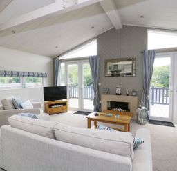 A living room with sofas a coffee table a television and glass doors opening to a balcony at 44 Heritage Park Stepaside near Kilgetty
