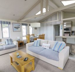 A living room with two sofas a wooden coffee table dining table with chairs and a kitchen with bar stools at 44 Heritage Park in Stepaside near Kilgetty