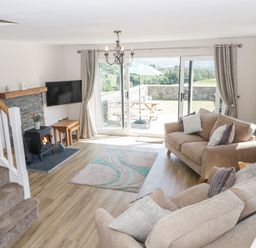 A living room with two sofas a fireplace a wall-mounted TV and sliding glass doors leading outside at Y Stabl in Llanddoged near Llanrwst