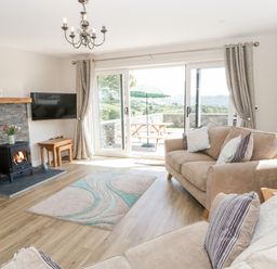 A living room with sofas a rug a wood burning stove and sliding doors leading to a patio at Y Stabl in Llanddoged near Llanrwst