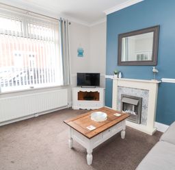 A living room with a wooden coffee table a fireplace with a mirror above and a TV on a corner unit at Sandy Toes Cottage in Newbiggin-By-The-Sea