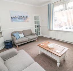 A living room with two sofas a wooden coffee table and a display cabinet at Sandy Toes Cottage in Newbiggin-By-The-Sea