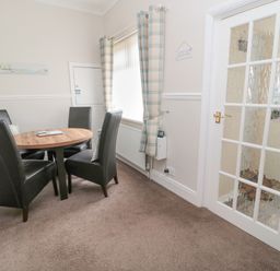 A dining area with a round wooden table and four black chairs beside a window with plaid curtains at Sandy Toes Cottage in Newbiggin-By-The-Sea