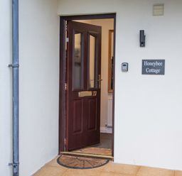 An open brown front door with number 27 and a doormat outside next to a wall with a Honeybee Cottage sign in Berrier near Penruddock