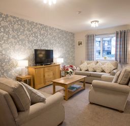 A living room with beige sofas a wooden coffee table a television and floral wallpaper at Honeybee Cottage in Berrier near Penruddock
