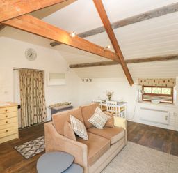 A living room with a sofa and cushions a small dining table with chairs exposed wooden beams a window with a blind and a kitchenette at The Coach House Merrion near Pembroke