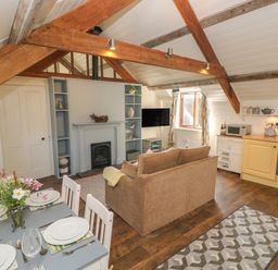 A dining table set with plates and cutlery in an open living room and kitchen with exposed wooden beams and a sofa at The Coach House in Merrion near Pembroke
