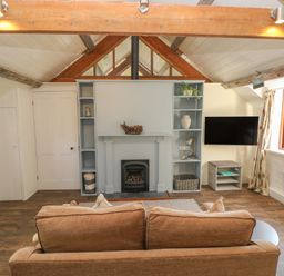 A living room with a brown sofa facing a fireplace and TV by a window at The Coach House Merrion near Pembroke