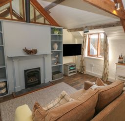 A living room with a brown sofa facing a blue fireplace with shelves and a TV near a window at The Coach House in Merrion near Pembroke