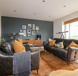 A living room with two black leather sofas and orange pillows at The Bolt Hole in Downderry