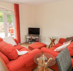 A living room with red sofas a glass coffee table a television on a glass stand and doors leading outside at Nuthatch Barn in Hensol near Pontyclun