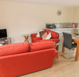 A living room with red sofas a wooden dining table with gray chairs and a small kitchen area at Nuthatch Barn in Hensol near Pontyclun
