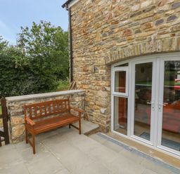 An outdoor patio with a wooden bench next to a stone wall and white double doors at Nuthatch Barn in Hensol near Pontyclun