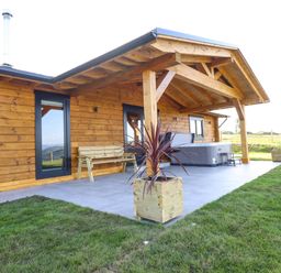 An outdoor patio area with a wooden bench hot tub two planters and two black chairs at Bacheiddon Log Cabin Aberhosan near Machynlleth