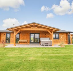 A wooden log cabin with a porch bench and hot tub on a tiled patio surrounded by grass at Bacheiddon Log Cabin Aberhosan near Machynlleth