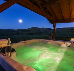 An outdoor covered hot tub with bubbling water towels bottle of champagne and glasses with hills in the background at Bacheiddon Log Cabin Aberhosan near Machynlleth