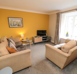 A living room with two beige sofas a yellow accent wall a television on a stand and a window with curtains at Esk Retreat in Whitby