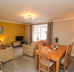 A living and dining room with beige sofas, a wooden dining table with chairs, and a television on a stand at Esk Retreat in Whitby