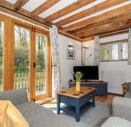 A sitting room with wooden beams grey sofas a blue coffee table and a television at Stow Cottage in Davidstow near Camelford