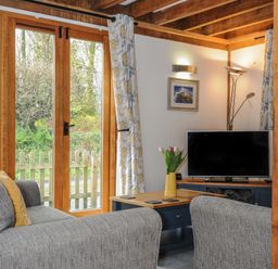 A living room with gray sofas a wooden coffee table a flat screen tv and large wooden framed glass doors at Stow Cottage in Davidstow near Camelford