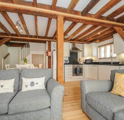 A living room with two grey sofas and a kitchen with white cabinets and wooden beams at Stow Cottage in Davidstow near Camelford