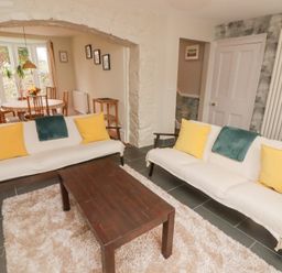A living room with two sofas with yellow pillows and a wooden coffee table next to a dining area with a round table and chairs at Morawel in Newport Pembrokeshire