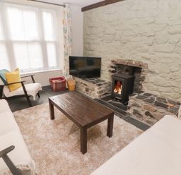 A living room with a stone wall fireplace wood stove sofas armchair wooden coffee table and large window at Morawel in Newport Pembrokeshire