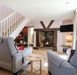 A sitting room with armchairs a wood burning stove and a staircase at Morawel Fach in Newport Pembrokeshire