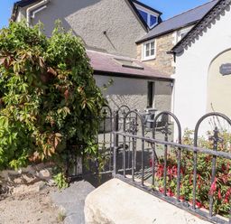The exterior of a house with a wrought iron fence a gate climbing plants and a patio with chairs at Morawel Fach in Newport Pembrokeshire